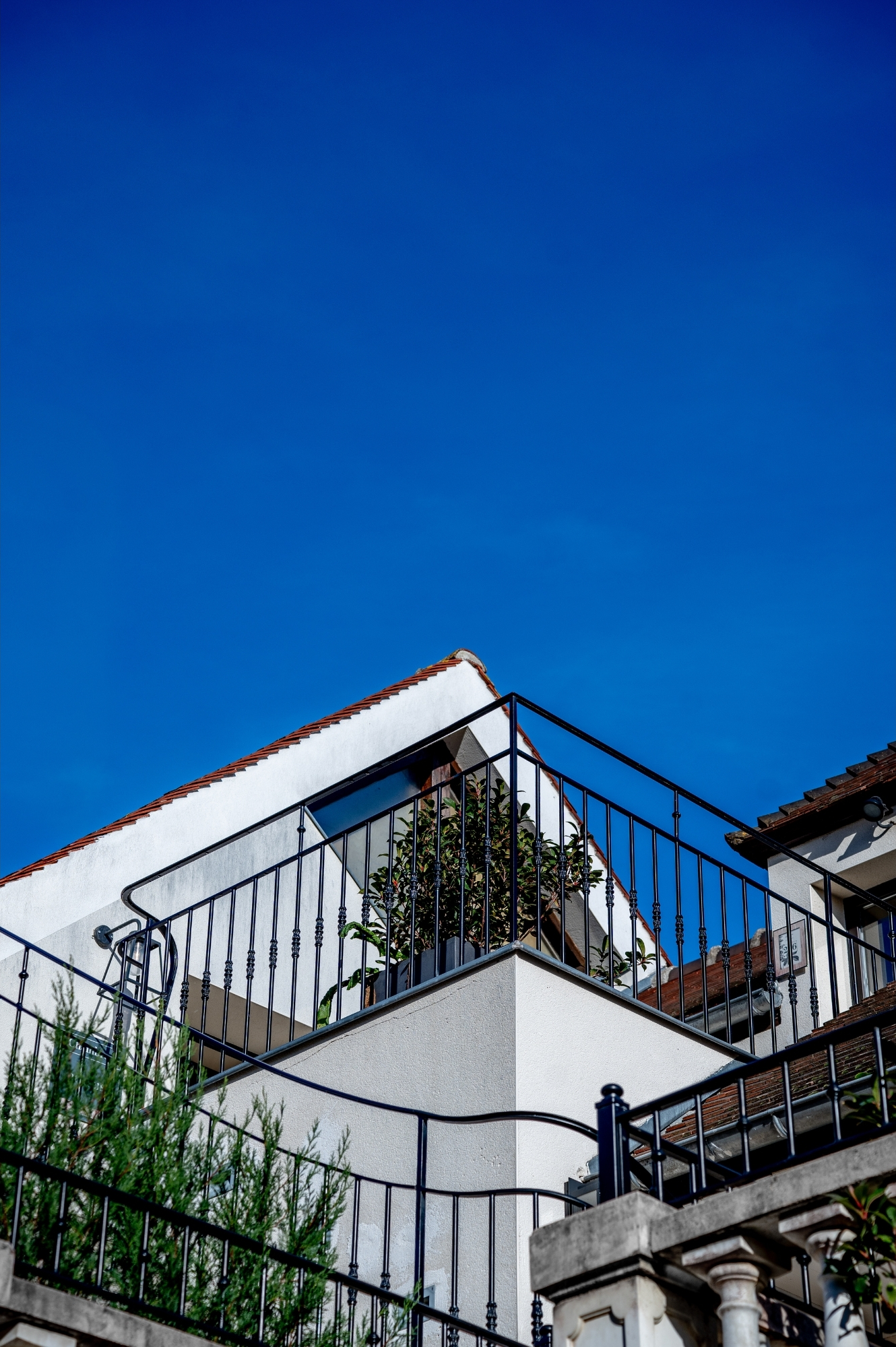 Toiture & balcon en fer forgé sous ciel bleu profond — détail architectural